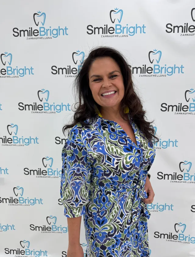 Eine Besucherin im gemusterten Kleid vor der Smile Bright Fotowand.
